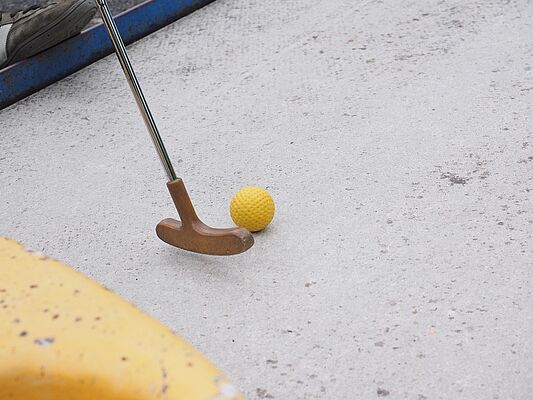 Minigolfschläger mit gelbem Ball auf Beton